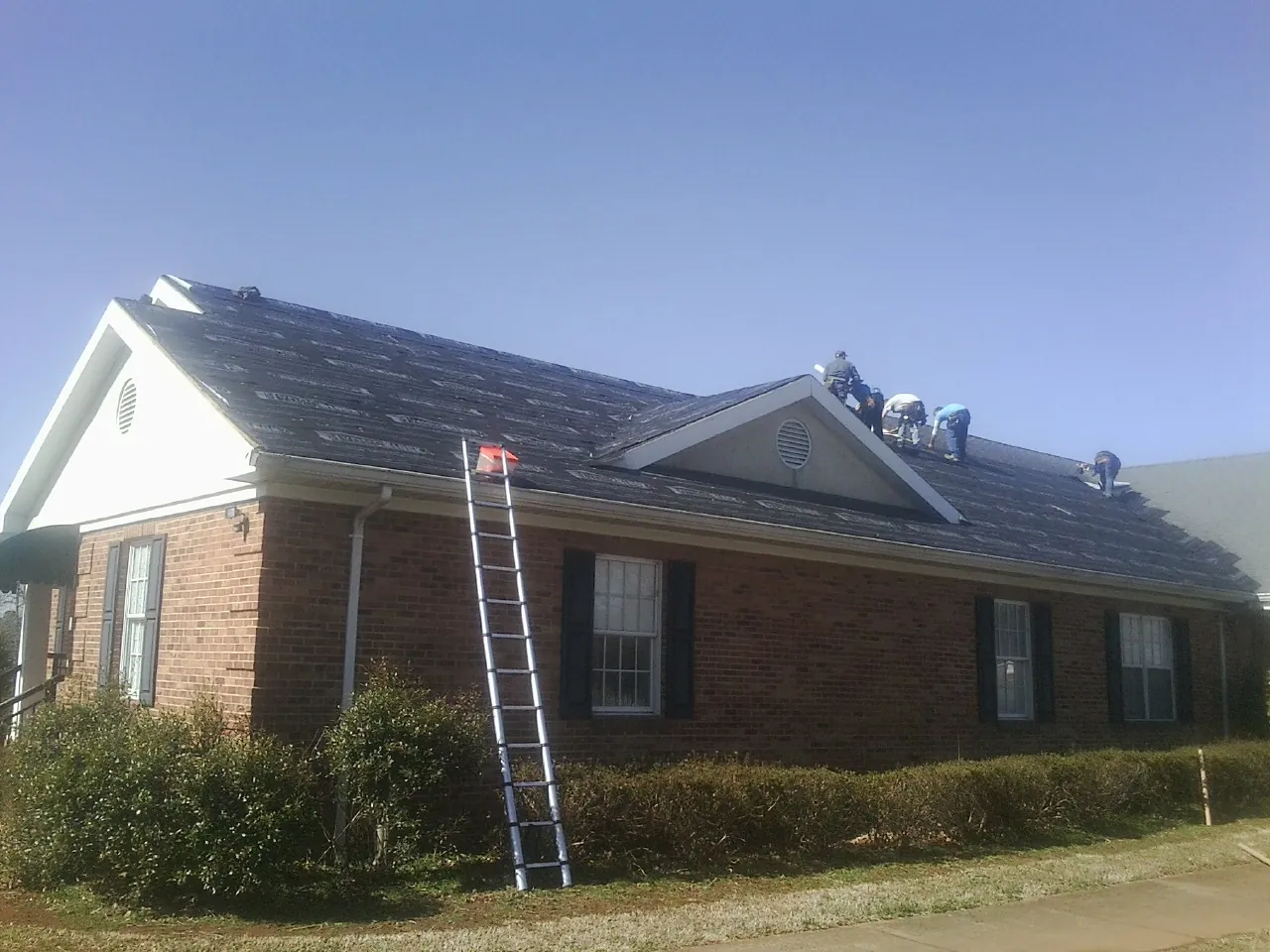 Crew tearing shingles off a brick ranch roof with a ladder set — Metal Roof Repair work by our crew in Canton